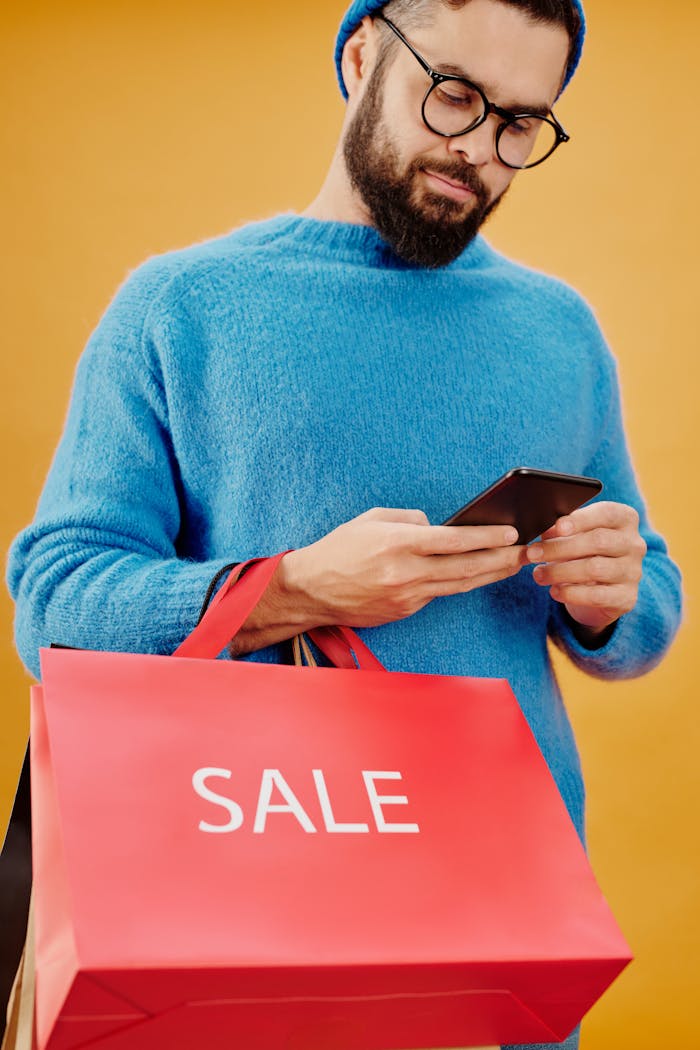 gallery-3 Bearded man holding a sale bag and smartphone in a studio setting.